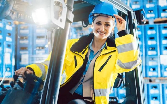 Woman driving a forklift in logistics delivery center looking into the camera